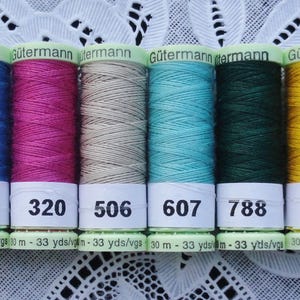 May include: Six spools of Gutermann thread in various colors: blue, pink, tan, turquoise, dark green, and yellow. Each spool has a white label with a number and the text "m - 33 yds/vgs".