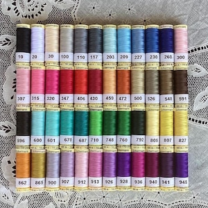 May include: A collection of colorful spools of Gutermann thread, arranged in neat rows. Each spool is labeled with a number, indicating the color. The threads are in various shades, including black, white, pink, red, and blue.