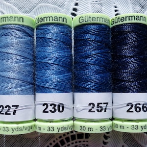 May include: Six spools of Gütermann thread in shades of blue, from light to dark. The spools are labeled with numbers 215, 227, 230, 257, 266, and 272. Each spool has a length of 33 yards.