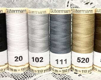May include: Six spools of Gütermann thread in black, white, silver, gray, beige, and brown. The spools are labeled with the numbers 10, 20, 102, 111, 520, and 590.