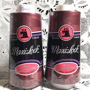 以下が含まれることがあります： マキシロックオールパーパススパンポリエステル糸の赤褐色の糸巻きが2つ。各糸巻きには「マキシロック」と「オールパーパススパンポリエステル」のラベルが貼られています。