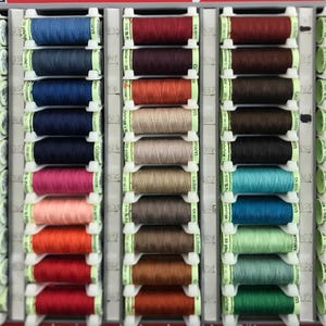 Puede incluir: Un organizador de hilo de coser lleno de carretes de hilo colorido. Los hilos son de varios tonos de azul, rojo, verde, amarillo y tonos neutros. Los carretes están cuidadosamente dispuestos en un organizador de plástico blanco.