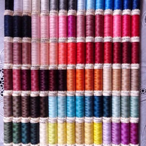May include: A collection of colorful sewing thread spools arranged in neat rows. The spools display a wide spectrum of colors, including shades of blue, pink, red, green, and yellow. The thread is wound on cylindrical spools, creating a visually appealing display.