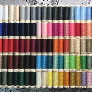 May include: A collection of 48 spools of 100% polyester thread in various colors. The spools are arranged in rows and are labeled with the brand name "Garn" and the text "100% Polyester".