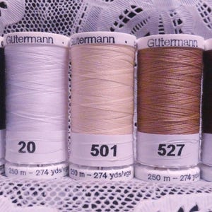 May include: Five spools of Gutermann thread in various colors: black, white, beige, brown, and dark brown. Each spool has a white label with a number and the Gutermann brand name. The thread is wound on cylindrical spools.
