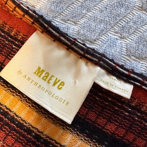 Puede incluir: Primer plano de un textil con una etiqueta que dice "Maeve by Anthropologie". El textil presenta un estampado de rayas en tonos naranja, amarillo y negro. La etiqueta tambi&eacute;n indica la talla XS y que est&aacute; hecho en Turqu&iacute;a.