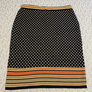 May include: A navy blue pencil skirt with a white polka dot pattern. The skirt has a striped design in orange, tan, and navy blue at the hem and waistband. The skirt is made of a knit fabric.