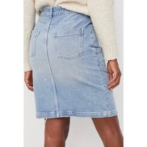 May include: Light blue denim skirt with a classic five-pocket design, featuring a back pocket, a small pocket on the front, and a side pocket. The skirt has white paint splatters and a button and zipper closure.
