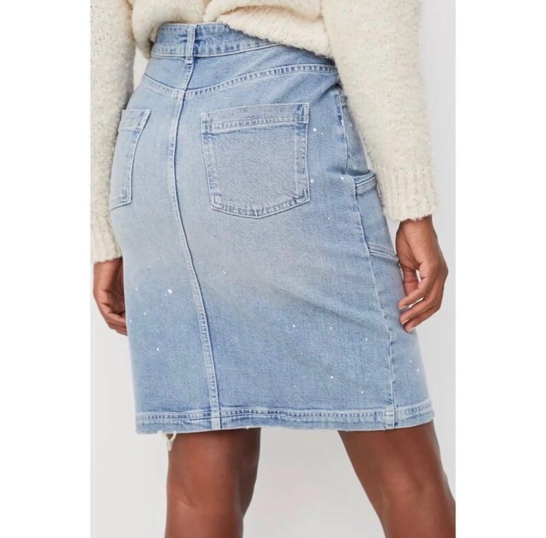 May include: Light blue denim skirt with a classic five-pocket design, featuring a back pocket, a small pocket on the front, and a side pocket. The skirt has white paint splatters and a button and zipper closure.