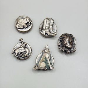 May include: A collection of five silver-toned metal pins with Western-themed designs. The pins feature a bison, cowboy boots, a cowboy riding a horse, a howling wolf, and a Native American chief.