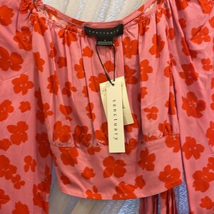 K&ouml;nnte beinhalten: Eine rosa Bluse mit langen &Auml;rmeln und rotem Blumendruck. Die Bluse hat einen quadratischen Ausschnitt und eine Schleife in der Taille. Das Etikett auf der Bluse lautet "sanctuary".