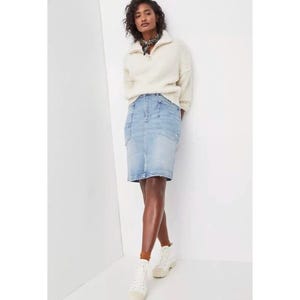 May include: A light blue denim pencil skirt with pockets. The skirt is paired with a cream-colored, zip-up sweater and white sneakers. The model is also wearing a patterned scarf.