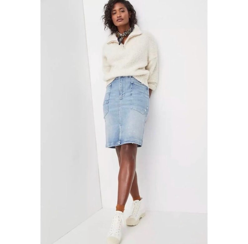 May include: A light blue denim pencil skirt with pockets. The skirt is paired with a cream-colored, zip-up sweater and white sneakers. The model is also wearing a patterned scarf.