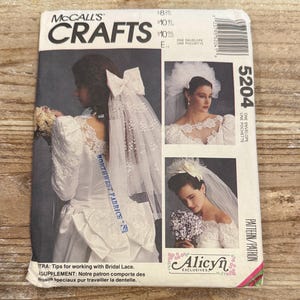 May include: A vintage McCall's Crafts pattern envelope featuring bridal designs. The cover showcases three images of brides in white wedding dresses with veils and lace details. The text includes "5204" and "Alicyn Exclusives".
