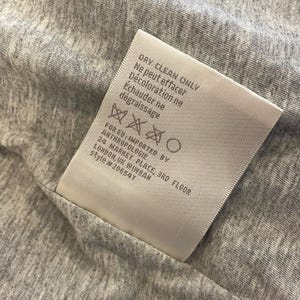 Op de afbeelding: Wit etiket met instructies voor alleen chemisch reinigen. Het etiket bevat ook de tekst "FOR EU: IMPORTED BY ANTHROPOLOGIE 24 MARKET PLACE, 3RD FLOOR LONDON, UK WIWBAN style #20654T".