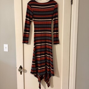 Puede incluir: Vestido midi de manga larga con cuello redondo. El vestido presenta rayas horizontales en negro, rojo, blanco y azul. El dobladillo es asim&eacute;trico, con un dise&ntilde;o de pa&ntilde;uelo. El vestido est&aacute; hecho de tejido de punto acanalado.