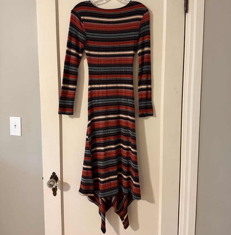 Puede incluir: Vestido midi de manga larga con cuello redondo. El vestido presenta rayas horizontales en negro, rojo, blanco y azul. El dobladillo es asim&eacute;trico, con un dise&ntilde;o de pa&ntilde;uelo. El vestido est&aacute; hecho de tejido de punto acanalado.