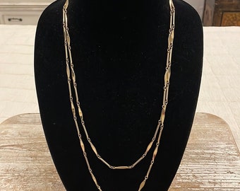 May include: A gold chain necklace with a delicate, elongated link design. The chain is layered twice, creating a longer, more substantial look.