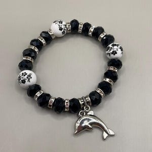 May include: Black and white beaded bracelet with a silver dolphin charm. The beads are black crystal and white ceramic with a floral design.