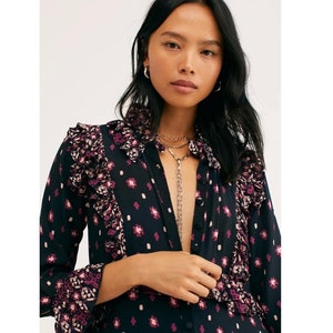 May include: A black and pink patterned long-sleeved shirt with a ruffled collar and cuffs. The shirt has a button-up front and a relaxed fit.