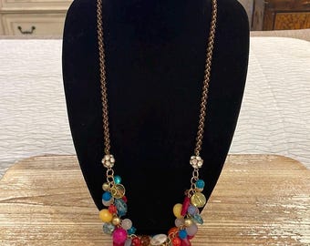 May include: A long, brown chain necklace with a cluster of colorful beads, including pink, red, orange, yellow, blue, green, and white. The beads are made of glass and have a variety of shapes and sizes.