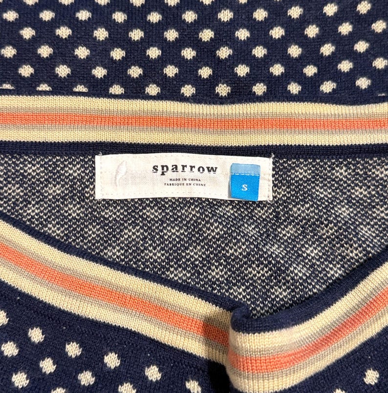 May include: Navy blue sweater with white polka dots and striped accents in cream and coral. The label reads "sparrow" and "S". Made in China.