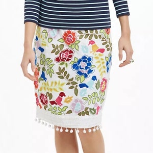 May include: White skirt with a colorful floral and bird print. The skirt has a white pom-pom trim.