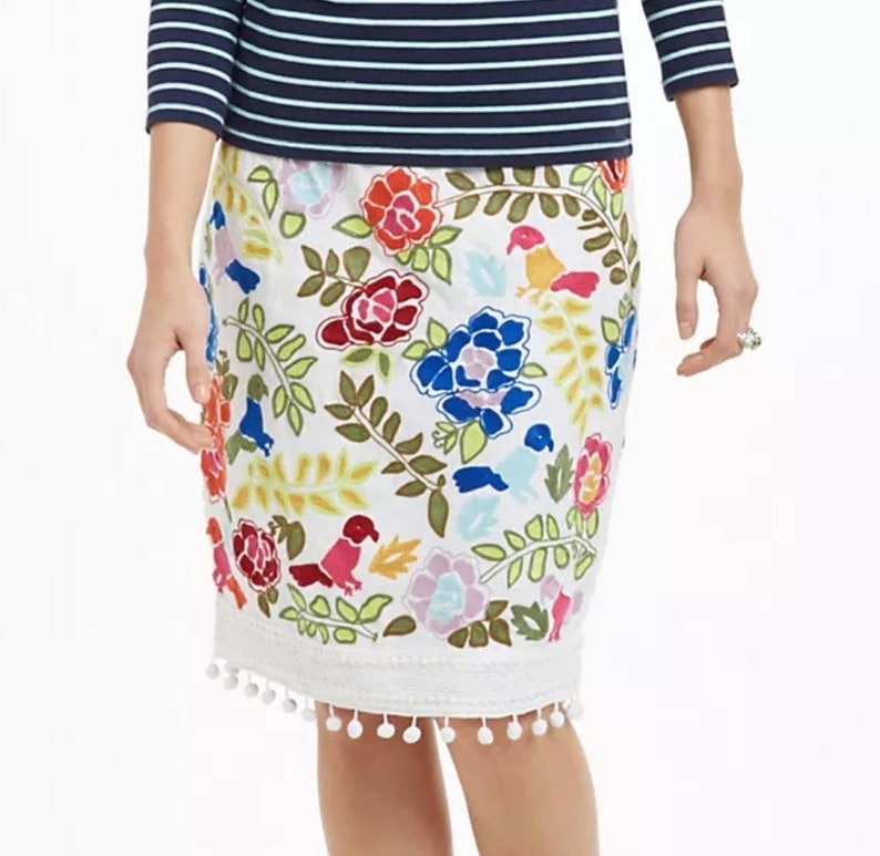 May include: White skirt with a colorful floral and bird print. The skirt has a white pom-pom trim.