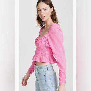 May include: A pink, long-sleeved, cropped blouse with a square neckline and a gathered, ruffled hem.