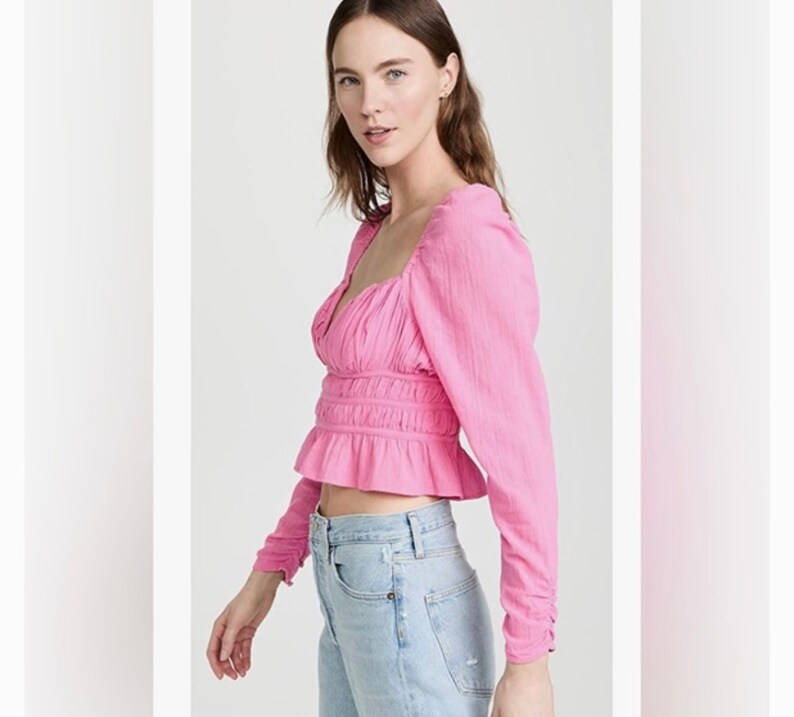 May include: A pink, long-sleeved, cropped blouse with a square neckline and a gathered, ruffled hem.