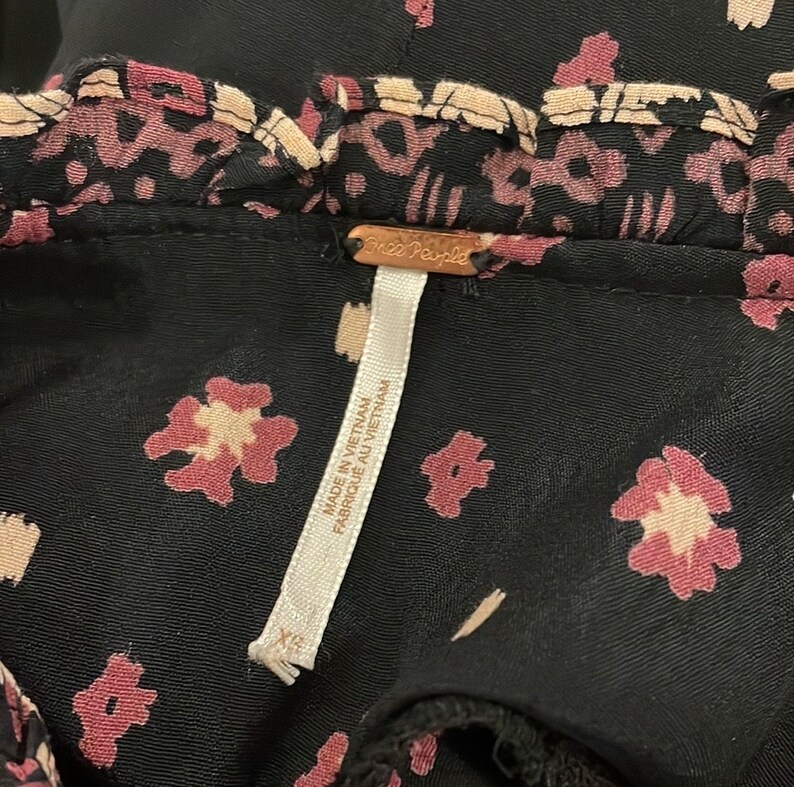 May include: Black floral print fabric with a Free People tag that reads "Made in Vietnam, Fabrique au Vietnam" and a size tag that reads "XS".