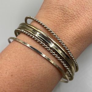 May include: A set of six gold-toned bangles, including a twisted rope design, a flat band, and a hammered band.
