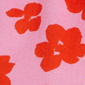 K&ouml;nnte beinhalten: Ein rosa Stoff mit einem sich wiederholenden Muster aus roten Blumen. Die Blumen sind stilisiert und haben ein einfaches Design.