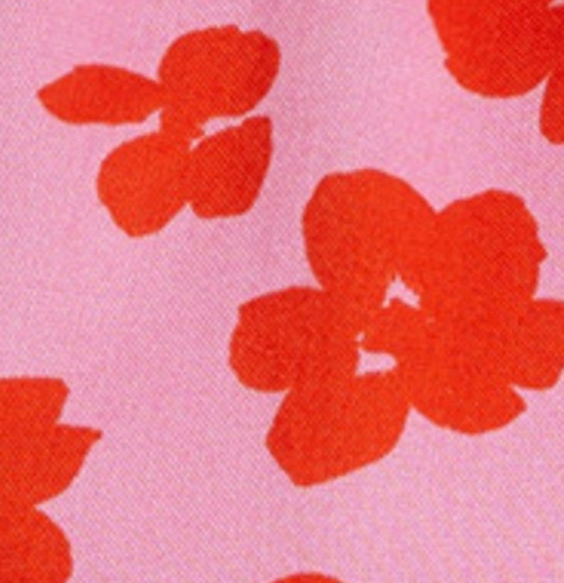 K&ouml;nnte beinhalten: Ein rosa Stoff mit einem sich wiederholenden Muster aus roten Blumen. Die Blumen sind stilisiert und haben ein einfaches Design.