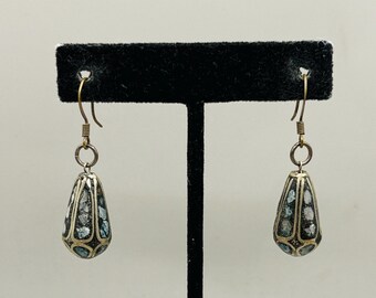 May include: A pair of silver-toned drop earrings with a teardrop shape. The earrings feature a mosaic design with blue and white accents. The earrings hang from gold-colored hooks.