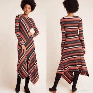 Puede incluir: Vestido de manga larga con estampado de rayas en tonos rojos, negros y blancos. El vestido tiene un dobladillo asim&eacute;trico y se combina con botas negras. La imagen muestra el vestido por delante y por detr&aacute;s.