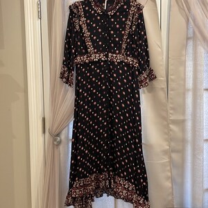 May include: A black maxi dress with a floral print and ruffled trim. The dress has a button-up front and long sleeves.