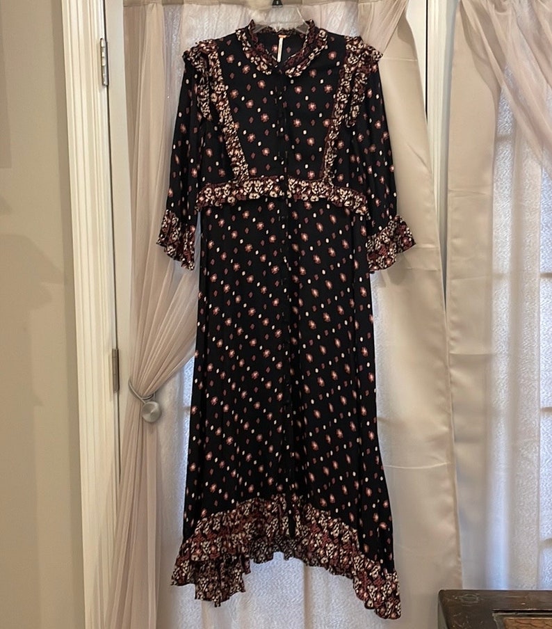 May include: A black maxi dress with a floral print and ruffled trim. The dress has a button-up front and long sleeves.