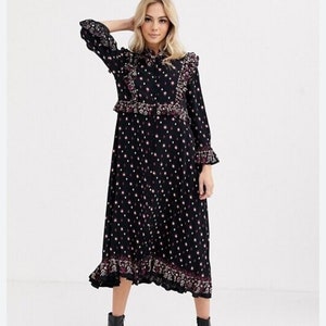 May include: A black midi dress with a white and pink floral print. The dress features a ruffled collar, ruffled cuffs, and a ruffled hem. The dress is knee-length and has a fitted bodice.
