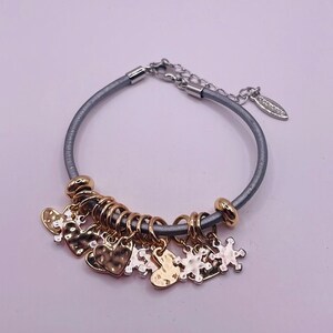 May include: A gray leather bracelet with a silver chain and multiple gold and silver charms, including hearts and snowflakes.