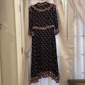 May include: A black maxi dress with a white and pink floral print. The dress has a ruffled neckline and sleeves, and a tiered skirt.