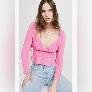 May include: A pink long-sleeved blouse with a gathered neckline and a fitted bodice. The blouse has a ruffled hem and is cinched at the waist.