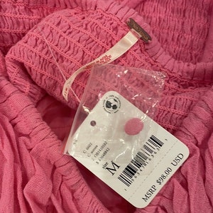May include: A pink Free People clothing tag with a white background. The tag has a barcode, the text "size M", and the text "MSRP $98.00 USD".