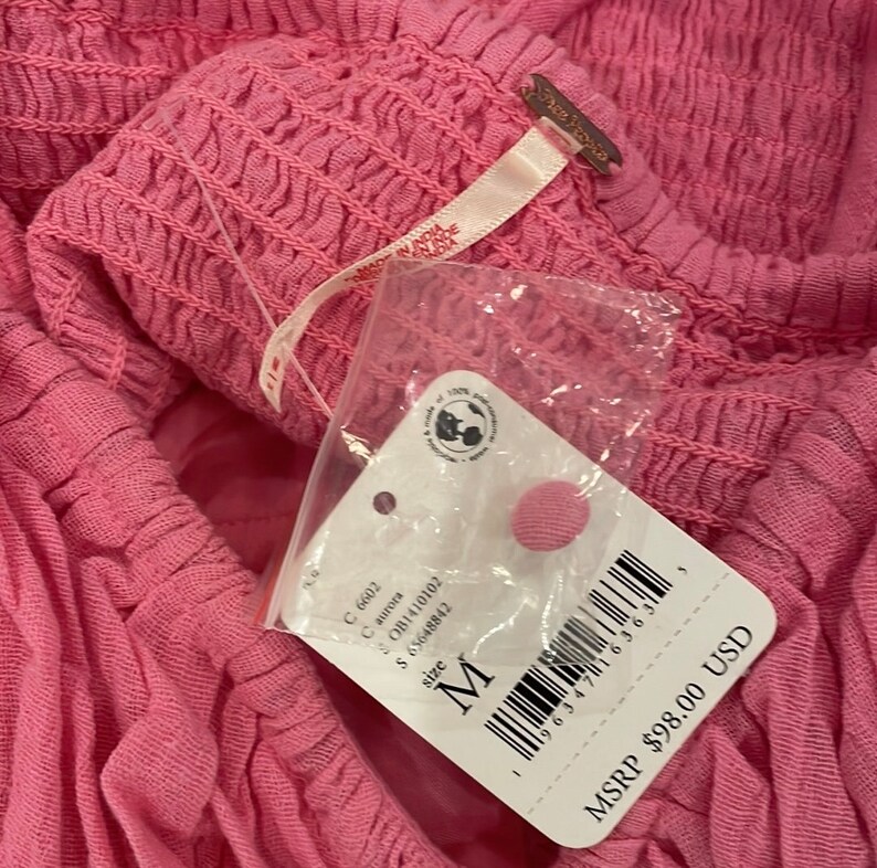 May include: A pink Free People clothing tag with a white background. The tag has a barcode, the text "size M", and the text "MSRP $98.00 USD".