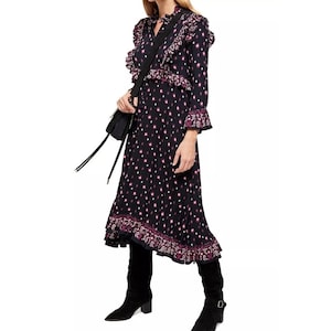 May include: A black midi dress with a pink floral print and ruffle detailing. The dress has a long sleeve and a high neck. The model is wearing black boots.