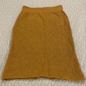 May include: A brown knitted skirt with a textured pattern. The skirt has a wide waistband and a slightly flared hem.