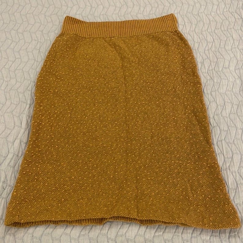 May include: A brown knitted skirt with a textured pattern. The skirt has a wide waistband and a slightly flared hem.