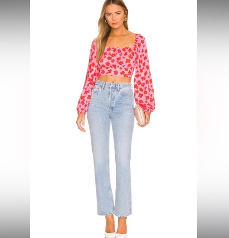 K&ouml;nnte beinhalten: Ein rosa-rotes, blumiges Crop-Top mit langen &Auml;rmeln, quadratischem Ausschnitt und figurbetonter Silhouette. Das Top wird mit einer hellblauen, hoch sitzenden Jeans kombiniert.