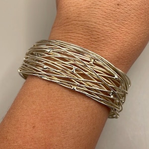 May include: A gold-toned bangle bracelet made of multiple thin, interwoven wires. The bracelet has a delicate, intricate design and features small, round accents.