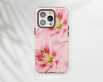 Puede incluir: Una funda de teléfono rosa y blanca con un diseño floral con lirios rosas. La funda tiene un borde negro y un recorte para la cámara.